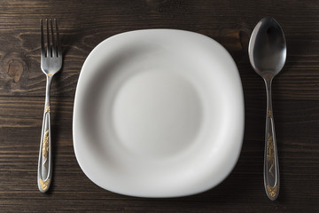  Fork, spoon and white plate on a dark wooden background