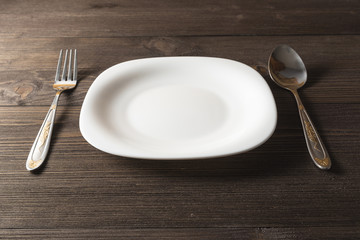  Fork, spoon and white plate on a dark wooden background