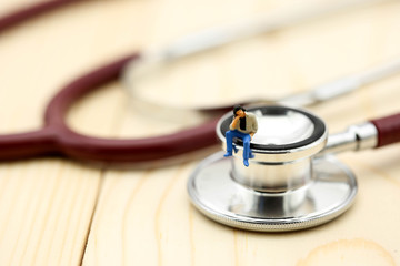 Miniature people : a man sitting with medical stethoscope,heathcare concept.