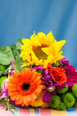 Sunflower and Gerbera in a bouquet of fresh vibrant brightly coloured florist flowers. Blue background. Copy space. Vertical. 