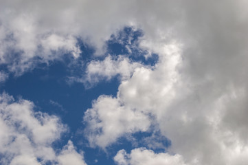 Cloudscape background, fluffy white clouds brightly back lit creating shadows and strong highlights, with a strong blue sky behind them. Beautiful, moody and atmospheric.