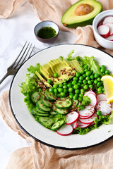 Mix salad with cucumber, avocado, green peas and flax seeds on a marble background