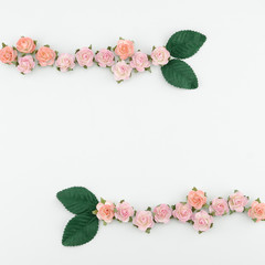 Pink and orange paper flowers and green leaves on white background with copy space