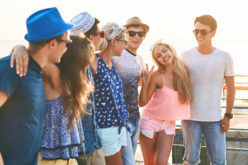 Group of happy carefree friends both young girls and men in casual clothes hanging out at the sunny summer seaside