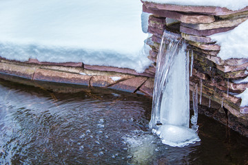Winter waterfall in the spring, ice stream of water in the lake. Rocks and snow.