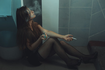Woman drug addict makes an injection sitting on a dirty floor. The problem of drug addiction in adolescents. - obrazy, fototapety, plakaty