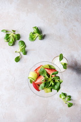 Spring summer diet salad with strawberries, cucumber, green field salad and yogurt mint sauce served in cocktail glass over grey texture background. Top view, space