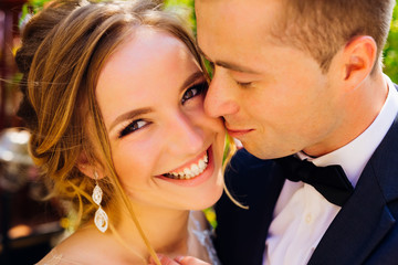 sincere smile of a beautiful bride looking at camera while groom touches her softly