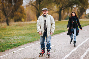 The old man goes on rollers with his daughter in the autumn park. Happy pension. Active old people.