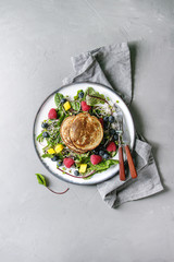 Vegan chickpea pancakes served in plate with green salad young beetroot leaves, sprouts, berries, berry sauce with cloth napkin, cutlery over grey concrete background. Top view, space. Healthy eating