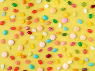 Many scattered colorful sweets, candies, lollipops on  bright yellow background, top view