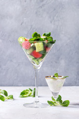Spring summer diet salad with strawberries, cucumber, green field salad and yogurt mint sauce served in cocktail glass over grey texture background. Copy space