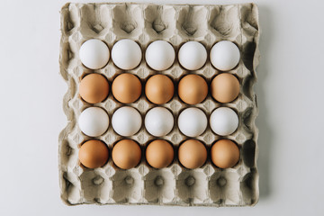 white and brown eggs laying in egg carton on white background