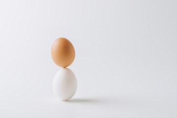 one white and one brown eggs stacked on white background