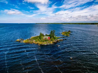 Zelfklevend Fotobehang A small red cottage on an island in the blue sea on a summer day. Finland. View from above. © nblxer