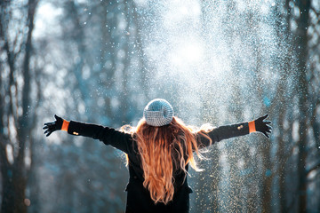 Fototapeta premium Young girl throwing snow in the air at sunny winter day, back view