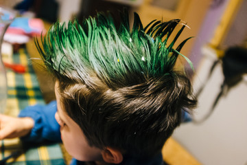 portrait of 9 year old boy at home with crest of green colored hair, performs funny gestures on the face with hands