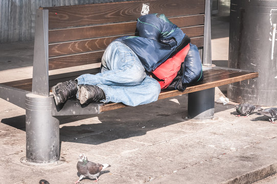 Homeless man, Poor homeless man or refugee sleeping on the wooden bench on the urban street in the city, social documentary concept