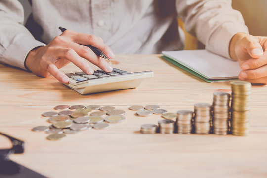 Business man or  accountant in gray shirt holding pen working on accounts and using  calculator and writing on desk, With sunset light.