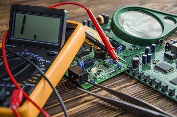 Multimeter and magnifying glass..Items are located on a brown wooden background, there are tweezers...