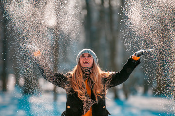 Smiling woman throwing snow in the air at sunny winter day