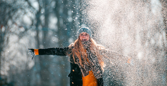 Smiling woman throwing snow in the air at sunny winter day