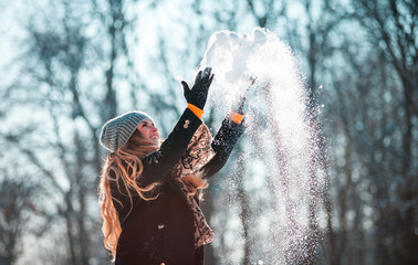 Smiling woman throwing snow in the air at sunny winter day