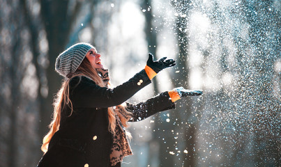 Fototapeta premium Smiling woman throwing snow in the air at sunny winter day