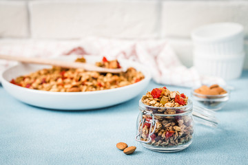 Honey almond granola in glass jar on light blue background. Selective focus, copy space.