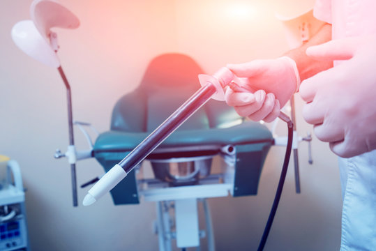 Proctologist holding an anoscope against a proctological chair.