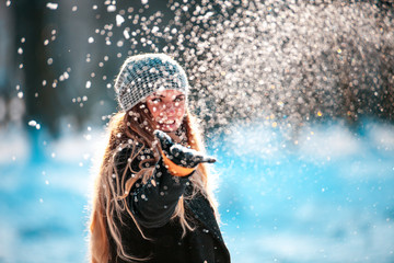 Obraz na płótnie Canvas Smiling young woman throwing snow in the air looking at camera