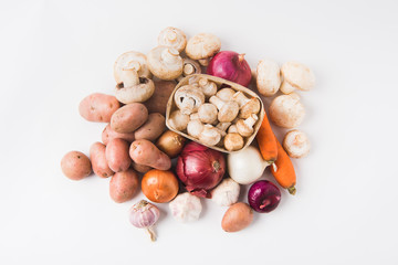 heap of mushrooms laying in basket over vegetables on white background