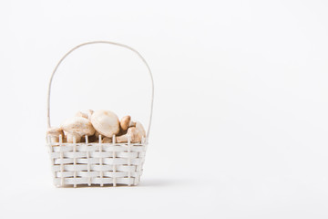 heap of champignon mushrooms laying in wicker basket on white background