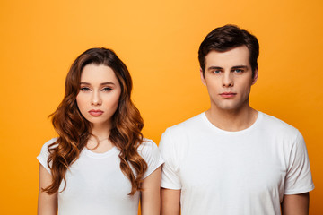 Photo of unhappy boyfriend and girlfriend in white t-shirts posing on camera with serious look,...