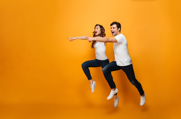 Fototapeta na wymiar Photo of energetic beautiful couple posing together on camera while running or jumping and pointing fingers on copyspace, along background
