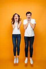 Fototapeta premium Full-length photo of amusing man and woman in casual posing together while jumping with hands on face, isolated over yellow background