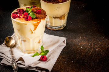 Three portioned glass with Italian dessert Tiramisu, with mint and raspberries, on dark rusty background.  Copy space