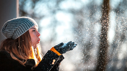 Winter woman blowing snow outdoor at sunny day, flying snowflakes