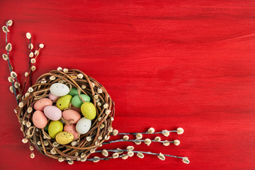 Obraz na płótnie Canvas Red Easter background. Easter willow wreath and colorful Easter eggs on red background. Top view, copy space. Greeting card
