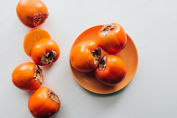 top view of persimmons on orange plate and on white tabletop