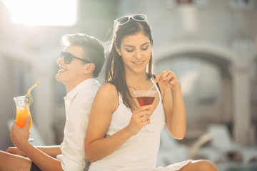Two attractive people having cocktails by the pool in the summer vacation resort.Pool lounge bar party.Couple on exotic travel vacation enjoying refreshing drinks and relaxing day.Friends having fun