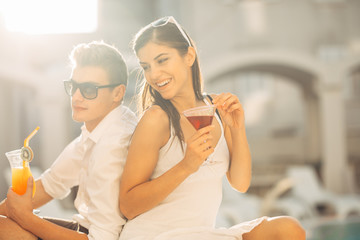 Two attractive people having cocktails by the pool in the summer vacation resort.Pool lounge bar party.Couple on exotic travel vacation enjoying refreshing drinks and relaxing day.Honeymoon vacation