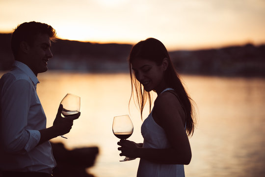 Two young people enjoying a glass of red wine in the sunset on the seaside.Healthy glass od homemade red wine,Mediterranean culture.Warm climates,seaside living couple.Seaside vacation experience