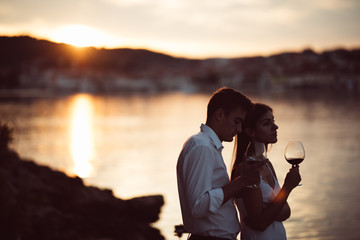 Two young people enjoying a glass of red wine in the sunset on the seaside.Healthy glass od...