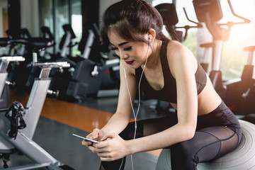 Beautiful young sportswoman listening music with cell phone in gym