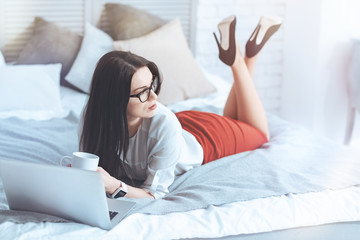 Pensive mood. Young business woman having a cup of coffee while relaxing on a bed and thinking about something.