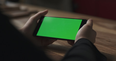female teen girl holding smartphone with green screen sitting at the table