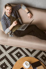happy handsome man with laptop sitting on couch