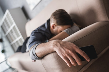 Fototapeta premium tired young man sleeping on couch with smartphone in hand