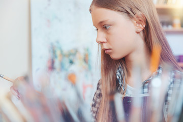 Magical activity. Teenage gill focusing her attention on an easel while painting and taking part in an art workshop.